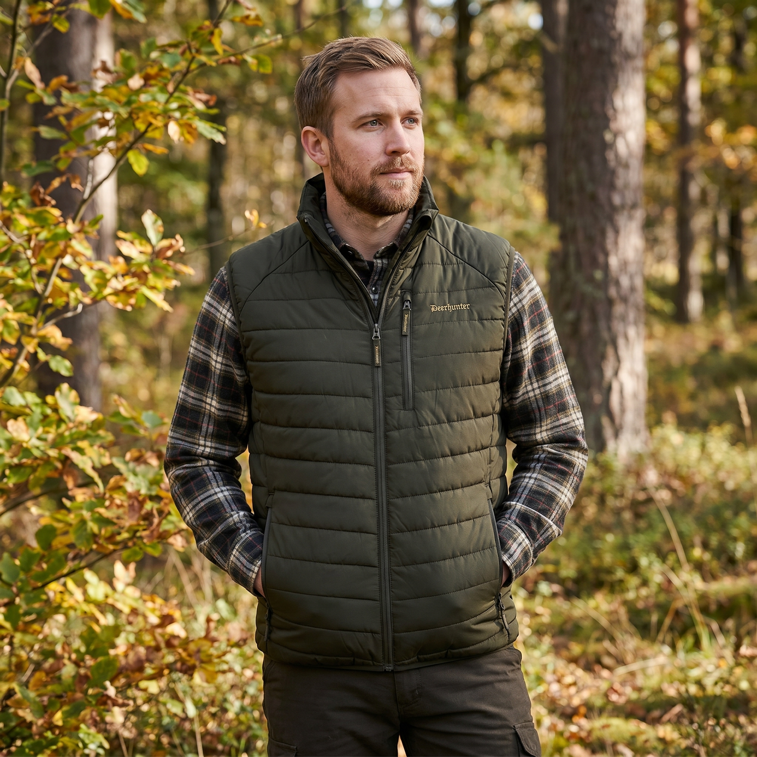 Man wearing a green puffer vest and plaid shirt in a forest setting
