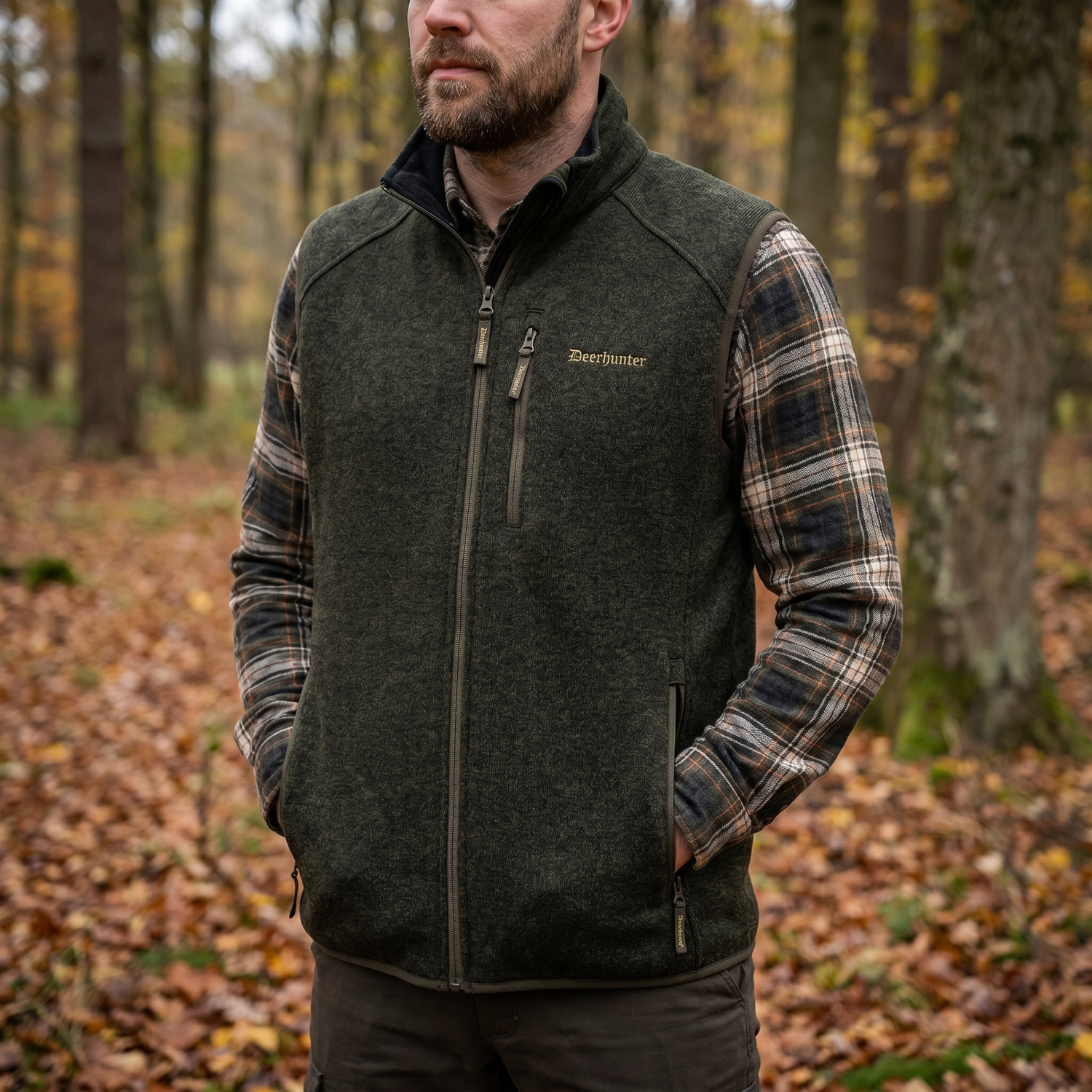 Man wearing a dark green vest with 'Beechfield' branding in an autumn forest setting.