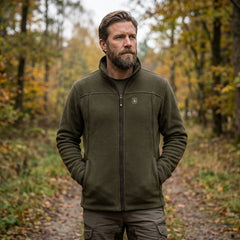 Man wearing a green jacket standing in a forest during autumn.