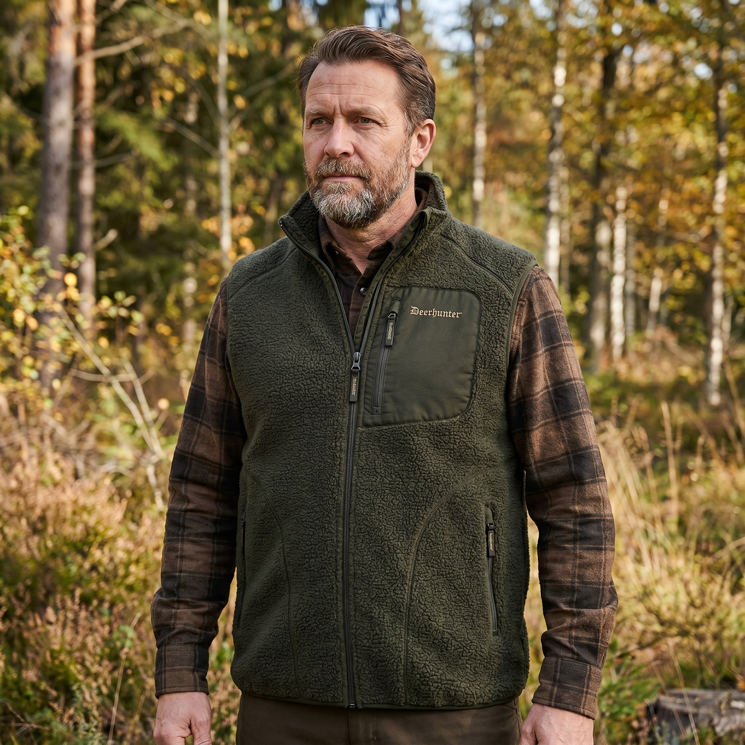 Man wearing a green fleece vest with plaid sleeves in a forest setting
