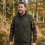 Man wearing a green fleece vest with plaid sleeves in a forest setting