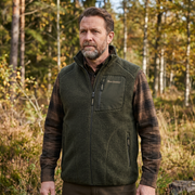 Man wearing a green fleece vest with plaid sleeves in a forest setting