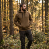 Man wearing a brown hoodie and dark pants standing in a forest