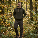 Man wearing a green hoodie and pants standing in a forest
