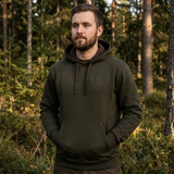 Man wearing a dark green hoodie standing in a forest