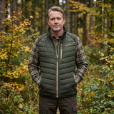 Man wearing a green puffer vest and plaid shirt standing in a forest.