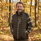 Man wearing a quilted vest and plaid shirt in a forest setting