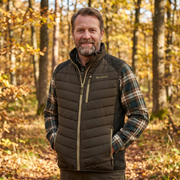 Man wearing a quilted vest and plaid shirt in a forest setting