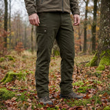 Person wearing green pants and a brown jacket in a forest setting